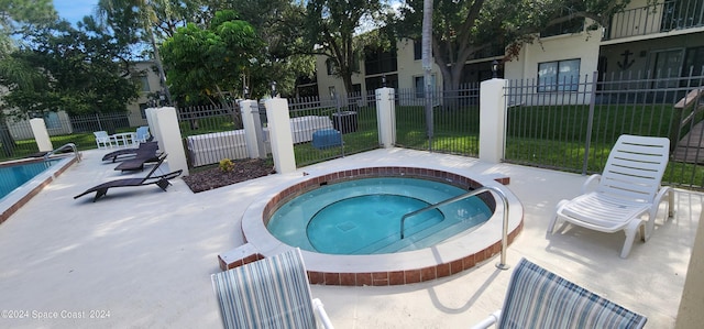 view of pool featuring a community hot tub, a fenced front yard, a patio, and a swimming pool