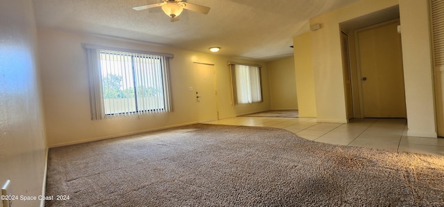 tiled empty room featuring a textured ceiling, carpet floors, ceiling fan, and baseboards