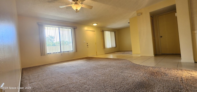 spare room featuring light colored carpet, baseboards, a textured ceiling, light tile patterned flooring, and ceiling fan