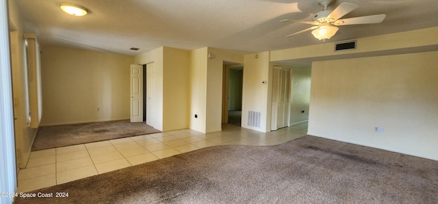 carpeted empty room with visible vents, ceiling fan, and tile patterned flooring