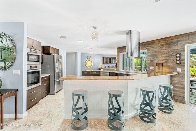 kitchen featuring kitchen peninsula, wood walls, appliances with stainless steel finishes, and a breakfast bar area