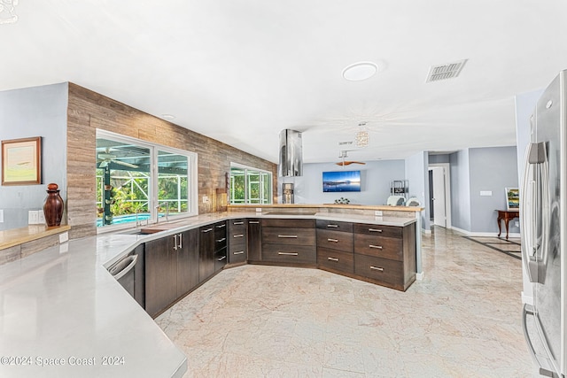 kitchen featuring stainless steel fridge, kitchen peninsula, wooden walls, and dark brown cabinetry