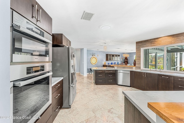 kitchen with kitchen peninsula, stainless steel appliances, sink, and dark brown cabinetry