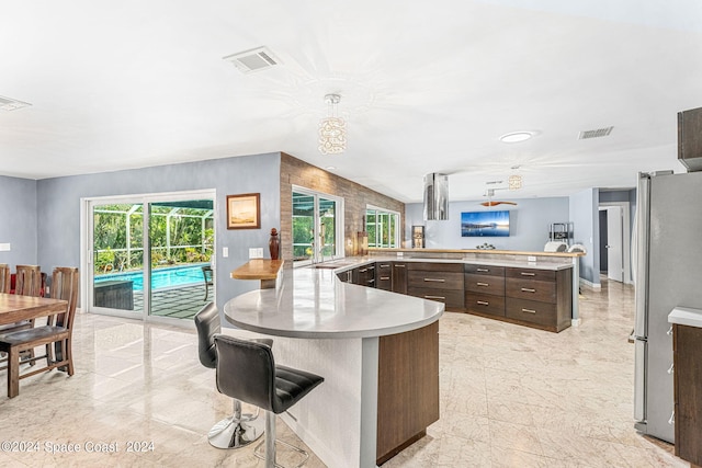 kitchen featuring decorative light fixtures, stainless steel refrigerator, kitchen peninsula, a kitchen bar, and dark brown cabinetry