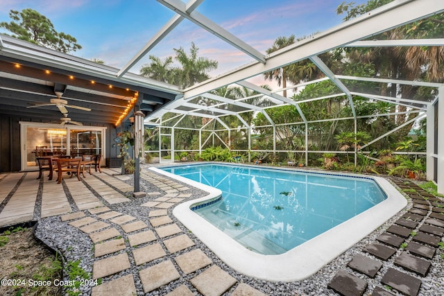 pool at dusk featuring glass enclosure, ceiling fan, and a patio