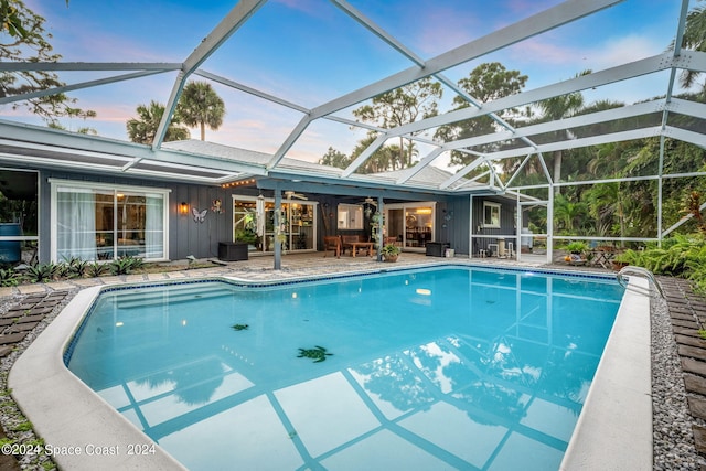 pool at dusk featuring a lanai and a patio area