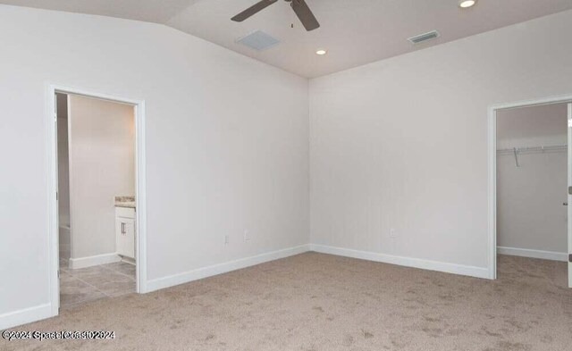 unfurnished bedroom featuring a walk in closet, vaulted ceiling, light colored carpet, a closet, and ceiling fan