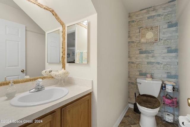 half bathroom with toilet, wooden walls, stone finish floor, and vanity