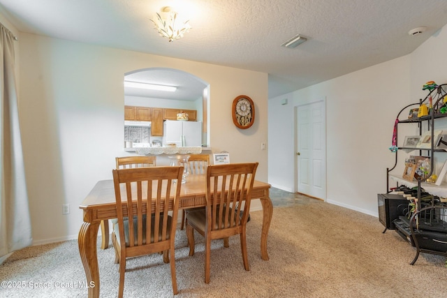 dining space featuring arched walkways, a textured ceiling, baseboards, and light colored carpet