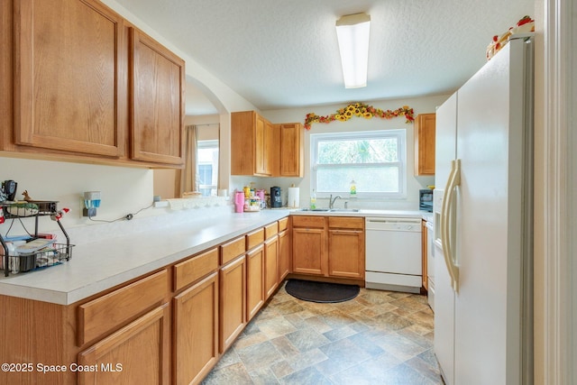 kitchen with light countertops, stone finish floor, a sink, a textured ceiling, and white appliances