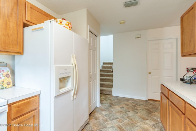 kitchen featuring white fridge with ice dispenser, light countertops, stone finish flooring, and visible vents