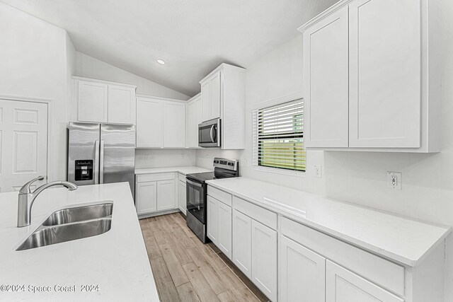 kitchen with white cabinets, sink, appliances with stainless steel finishes, light wood-type flooring, and vaulted ceiling