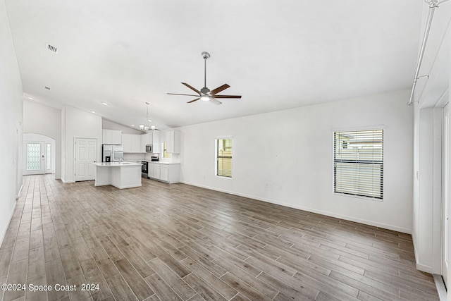 unfurnished living room featuring ceiling fan with notable chandelier, light hardwood / wood-style floors, and high vaulted ceiling