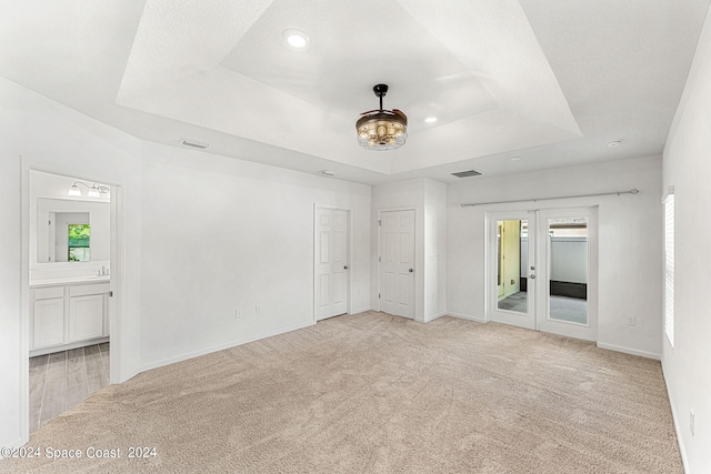 spare room with a raised ceiling, light carpet, and french doors