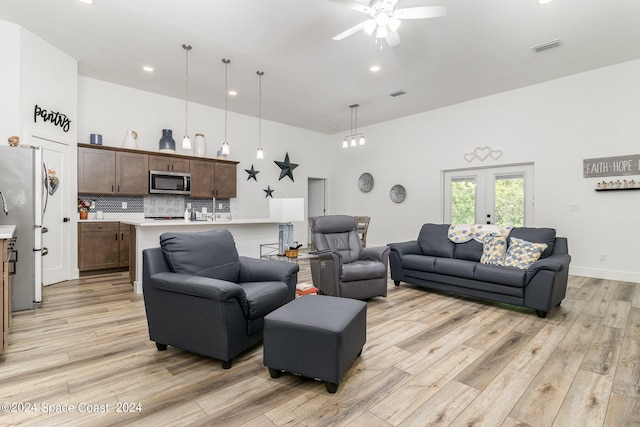 living room with light wood-type flooring, ceiling fan, and a towering ceiling