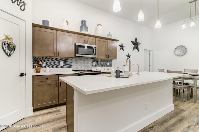 kitchen featuring light wood-type flooring, a kitchen island with sink, decorative light fixtures, sink, and appliances with stainless steel finishes