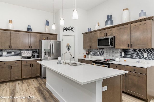 kitchen with stainless steel appliances, sink, wood-type flooring, an island with sink, and tasteful backsplash