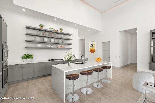 kitchen with light wood-type flooring, a kitchen bar, a high ceiling, and stainless steel oven