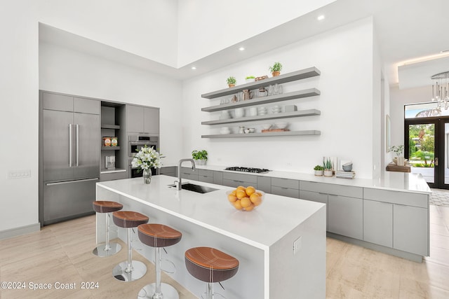 kitchen with a kitchen island with sink, gray cabinets, stainless steel appliances, a kitchen breakfast bar, and sink