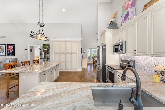 kitchen with dark wood-type flooring, light stone countertops, appliances with stainless steel finishes, decorative light fixtures, and a kitchen bar