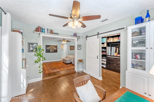 sitting room with a textured ceiling, a barn door, light hardwood / wood-style floors, and ceiling fan