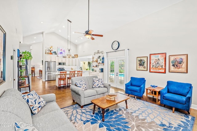 living room with hardwood / wood-style floors, ceiling fan with notable chandelier, high vaulted ceiling, and french doors