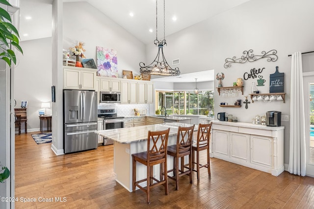 kitchen with high vaulted ceiling, a kitchen breakfast bar, sink, light wood-type flooring, and stainless steel appliances