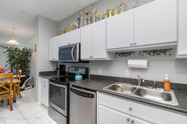 kitchen featuring stainless steel appliances, dark countertops, a sink, and white cabinetry