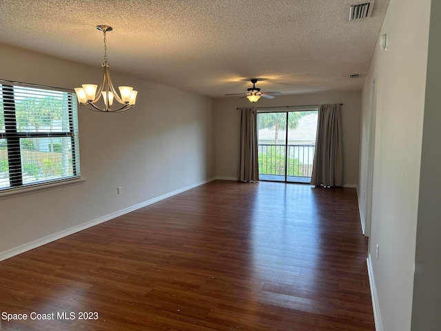 empty room featuring dark wood-type flooring, ceiling fan with notable chandelier, a wealth of natural light, and a textured ceiling