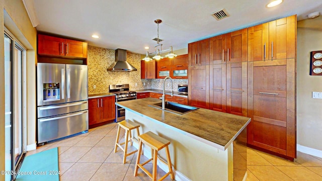 kitchen featuring a kitchen island with sink, tasteful backsplash, stainless steel appliances, sink, and wall chimney range hood