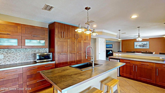 kitchen with sink, a kitchen breakfast bar, an island with sink, ceiling fan, and tasteful backsplash