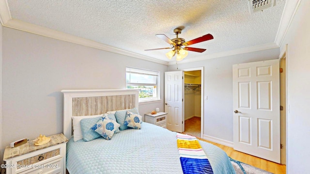 bedroom featuring crown molding, a walk in closet, a closet, ceiling fan, and a textured ceiling