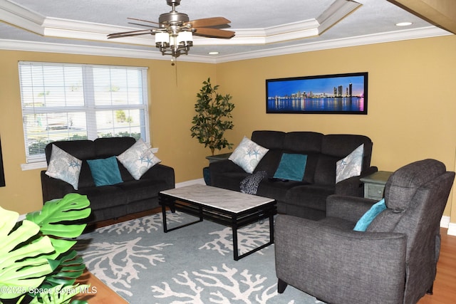 living area with ceiling fan, a raised ceiling, wood finished floors, and ornamental molding