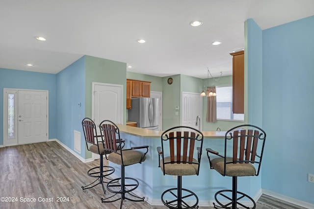 kitchen with light wood-type flooring, a breakfast bar area, kitchen peninsula, an inviting chandelier, and stainless steel fridge