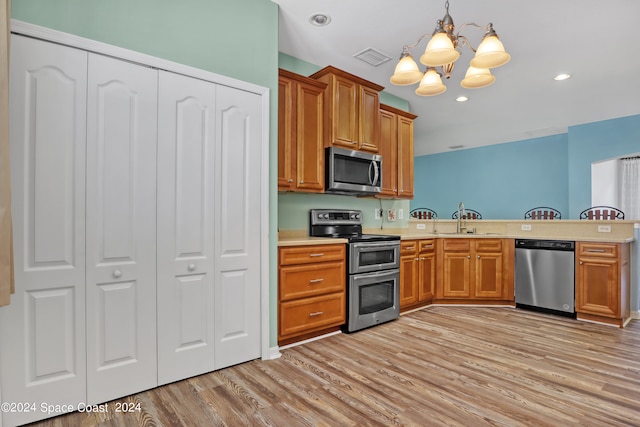 kitchen with light hardwood / wood-style floors, stainless steel appliances, decorative light fixtures, sink, and a notable chandelier