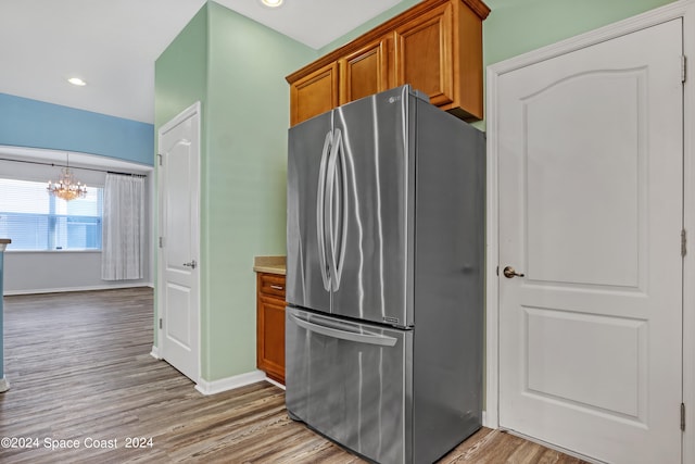 kitchen featuring pendant lighting, wood-type flooring, a chandelier, and stainless steel refrigerator