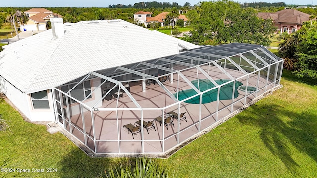 rear view of house with glass enclosure, a yard, and a patio