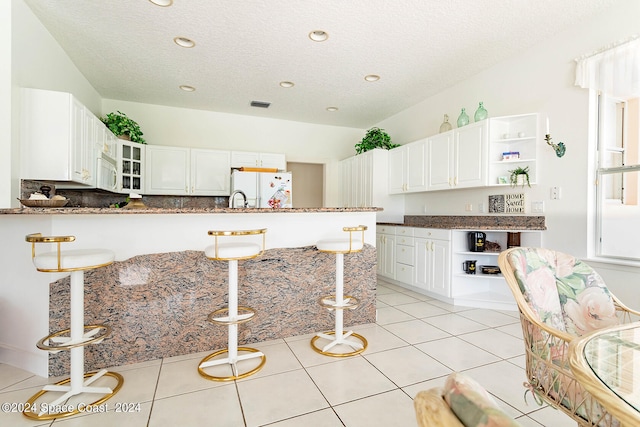 kitchen with white appliances, kitchen peninsula, light tile patterned floors, and a textured ceiling