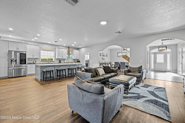 living room featuring light wood-type flooring, a chandelier, and a textured ceiling