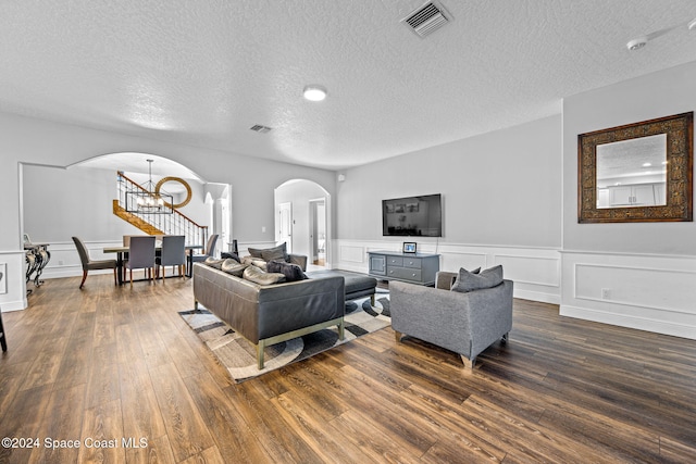 living room with dark wood-type flooring, a textured ceiling, and an inviting chandelier