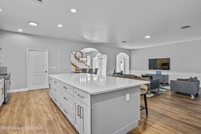 kitchen with white cabinetry, gas stove, a kitchen bar, wood-type flooring, and a center island