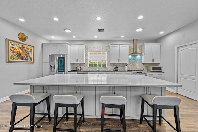 kitchen with stainless steel appliances, a kitchen bar, wall chimney range hood, and a large island