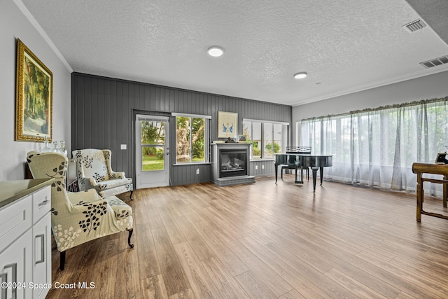 sitting room with wood walls, a textured ceiling, light hardwood / wood-style floors, and crown molding