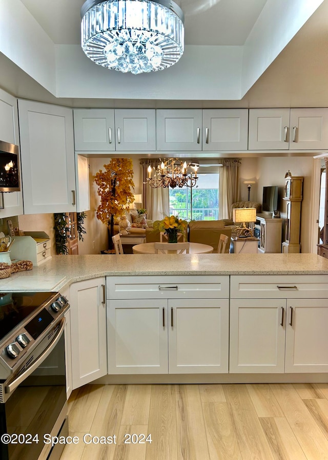 kitchen with appliances with stainless steel finishes, light hardwood / wood-style flooring, white cabinetry, a raised ceiling, and a notable chandelier