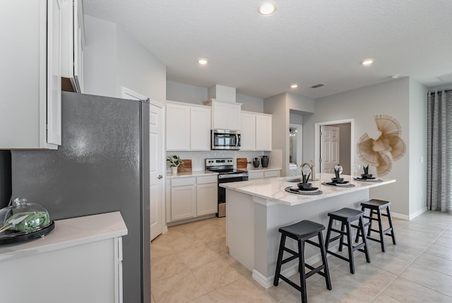 kitchen with a breakfast bar, visible vents, white cabinetry, appliances with stainless steel finishes, and a center island with sink