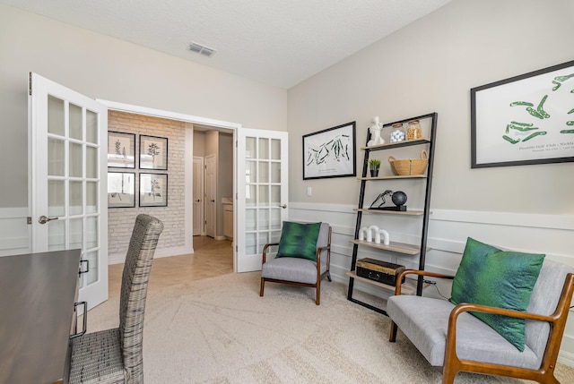 office area featuring a textured ceiling, light colored carpet, brick wall, visible vents, and french doors