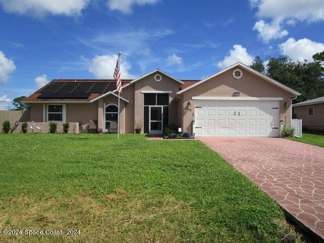 ranch-style house with a front lawn, solar panels, and a garage