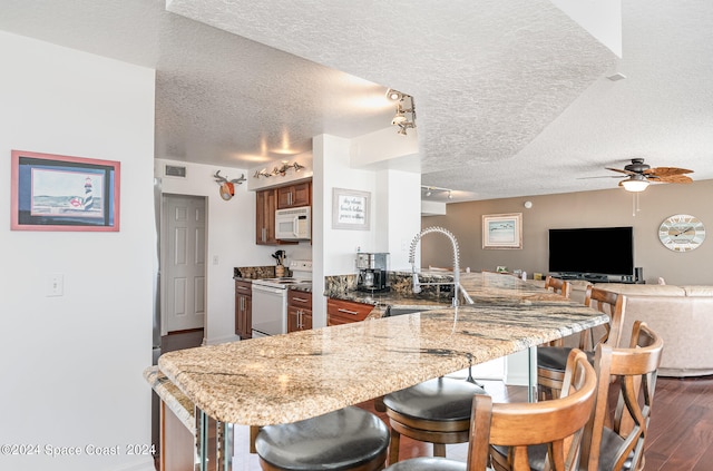 kitchen featuring a textured ceiling, dark wood-type flooring, kitchen peninsula, and white appliances