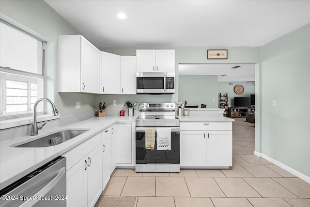 kitchen with light tile patterned floors, kitchen peninsula, sink, appliances with stainless steel finishes, and white cabinets