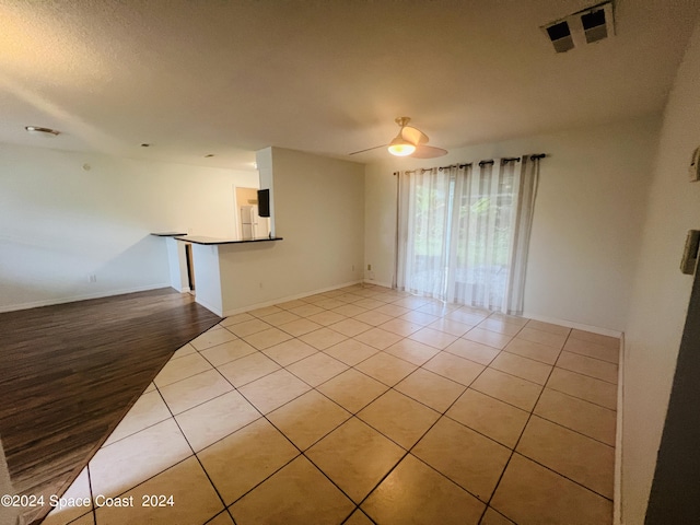 empty room featuring visible vents, a ceiling fan, a textured ceiling, baseboards, and tile patterned floors